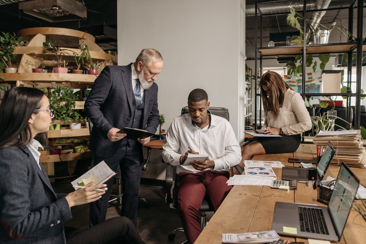 A diverse group of coworkers meeting in a contemporary office, working together on projects with technology and documents.